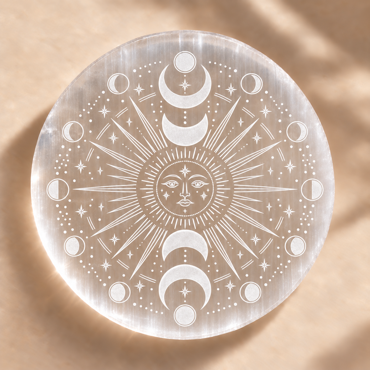 Selenite charging plate with an engraved sun face, stars and moon phases on a warm beige background.