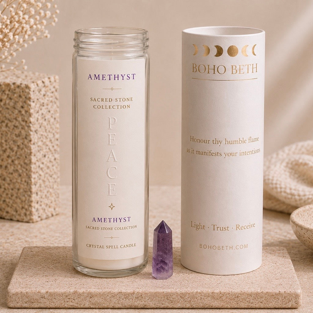 A glass jar candle labeled 'AMETHYST SACRED STONE COLLECTION PEACE' stands beside its white cylindrical packaging tube printed with 'BOHO BETH' and moon phase graphics, set on a stone slab with neutral decorative props.