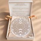 Selenite charging plate with celestial engraving in a cream gift box with gold usage instructions.