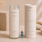 A glass jar candle labeled FLUORITE from the BOHO BETH Sacred Stone Collection stands next to its white cylindrical packaging box and a small amethyst crystal point on a neutral beige background.